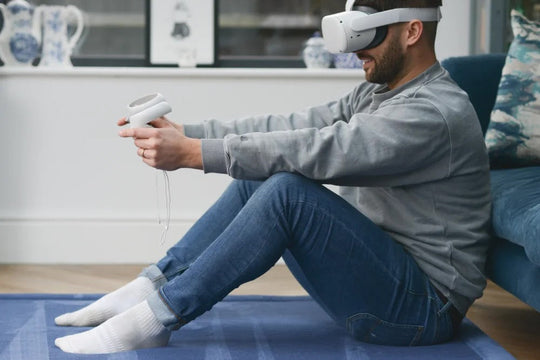 Man wearing a VR headset and holding controllers while sitting on a blue Momomi play mat in a living room