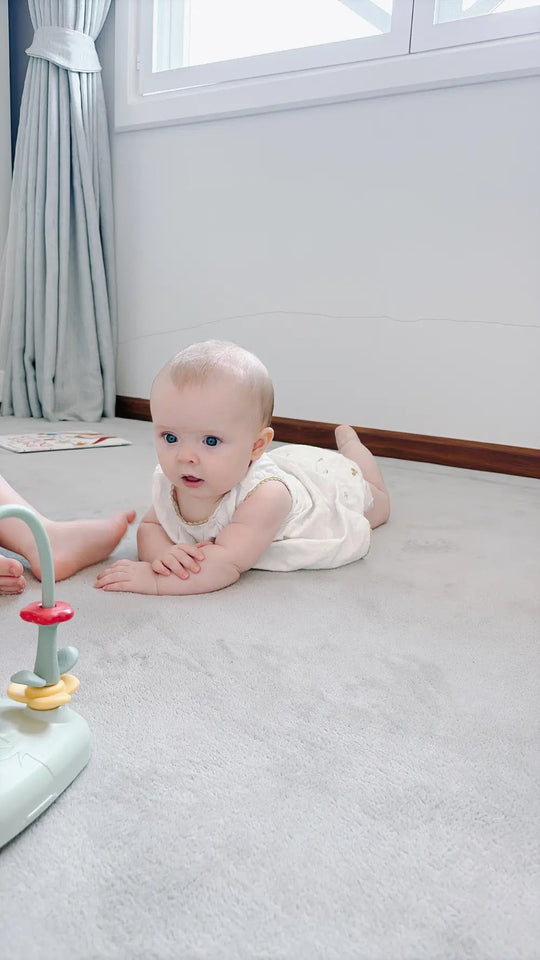 Baby doing tummy time on a soft cream sensory mat beside a stacking-ring toy in a bright room