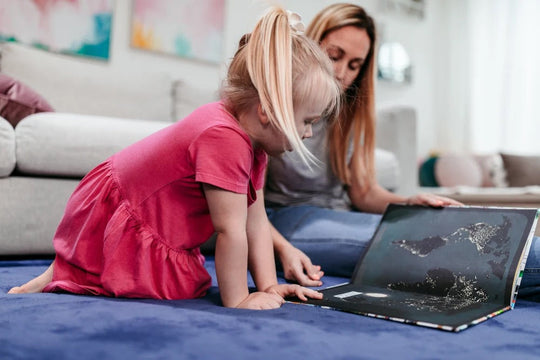 Young girl and mother looking at a picture book together on a navy foam play mat