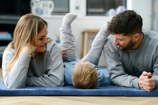 Mum, dad and their toddler playing together on a plush navy Momomi nursery rug