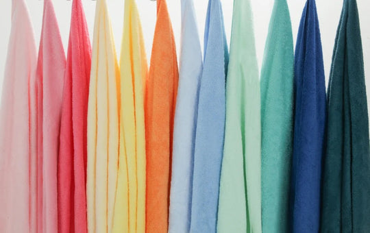 Row of Momomi Happy Towels hung side by side in a full rainbow of colours against a white wall